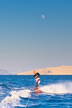 Wakeboarder in wetsuit riding in sunset. Wakeboarding is a surface water sport which involves riding a wakeboard over the surface of a body of water.