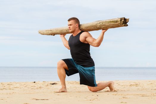 Sport, fitness. Bodybuilder with a big wood on the beach