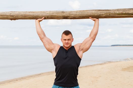 Sport, fitness. Bodybuilder with a big wood on the beach