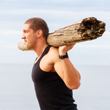 Sport, fitness. Bodybuilder with a big wood on the beach