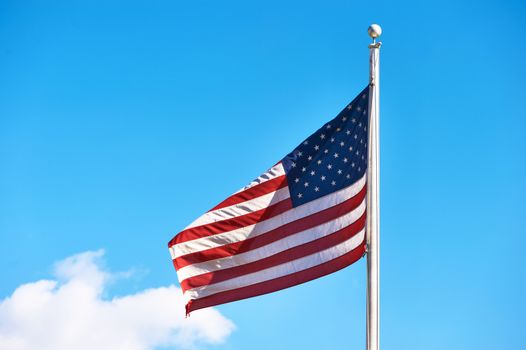 US American flag waving in the wind against blue sky and clouds