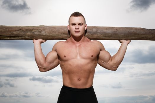 Sport, fitness. Bodybuilder with a big wood on the beach