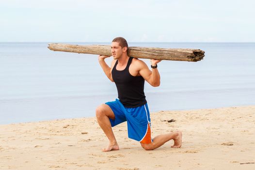 Sport, fitness. Bodybuilder with a big wood on the beach