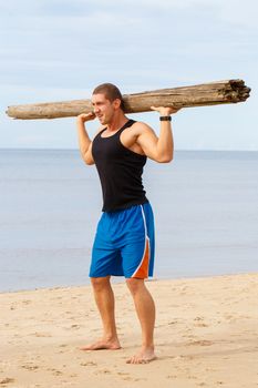 Sport, fitness. Bodybuilder with a big wood on the beach