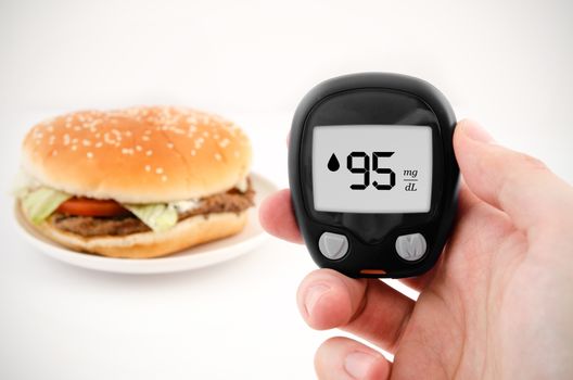 Hand holding meter. Diabetes doing glucose level test. Hamburger in background