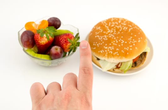 Finger choosing between hamburger and fruits. Food on white background