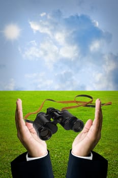 Binocular in businessman hand with field background