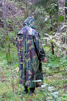 A man in a camouflage hooded standing back in the woods with a knife in his hand               