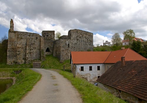 Photo shows main view of an old castle with red roof houses around.