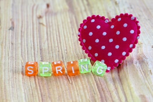 Photo shows details of spring sign with heart on the wooden background.