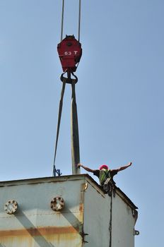 A worker high up on a structure being demolished, communicates with the crane operator down below, by means of hand signals and gestures.