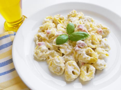 Italian cuisine background. Delicious stuffed pasta tortellini with cream, ham and basil on white dish.