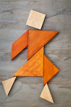 abstract of a dancing or walking figure built from seven tangram wooden pieces, a traditional Chinese puzzle game; slate rock background background, the artwork copyright by the photographer