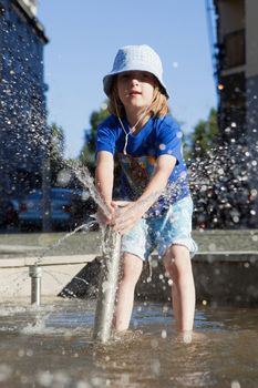 Boy in Cap Squirting Water from Fountain in Outdoor Pool