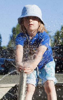 Boy in Cap Squirting Water from Fountain in Outdoor Pool