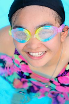 Young girl smiling and having fun swimming in a pool with blue water