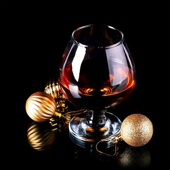 Glass with drink and a Christmas balls on a black background. New Year's balls and glass. Glass with alcohol and a Christmas ball.