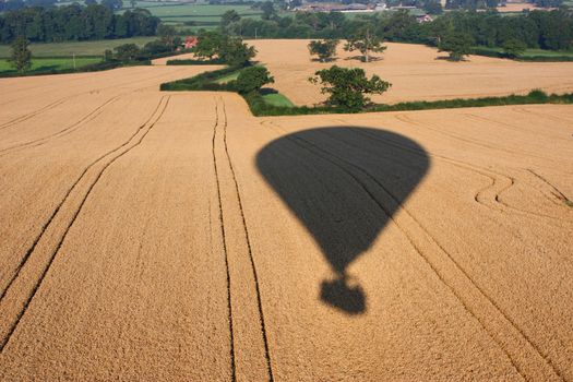 Shadow of a hot air balloon flying over rural farmland