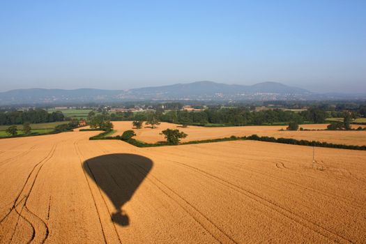 Shadow of a hot air balloon flying over rural farmland