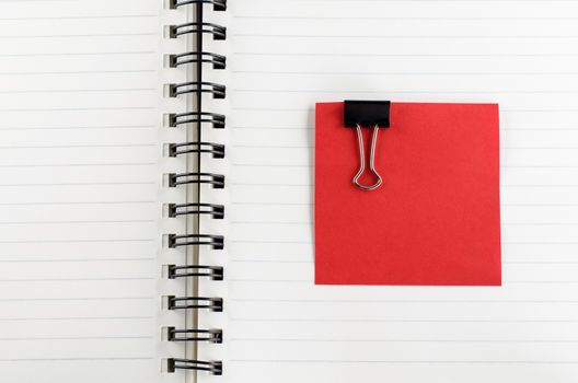 red paper note with black clip on notebook