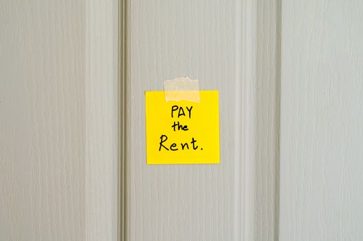 sticky note write a message pay the rent on wood door background