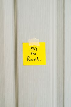 sticky note write a message pay the rent on wood door background