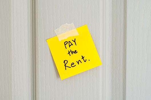 sticky note write a message pay the rent on wood door background