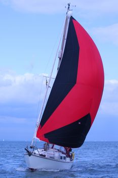 yacht sailing with a red and black spinnaker on the solent