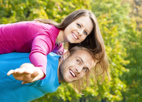 happy young couple piggybacking, arms outstretched, smiling.