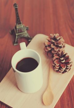 Black coffee and spoon on wooden tray with pine cone, retro filter effect 