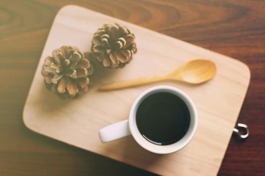 Black coffee and spoon on wooden tray with pine cone, retro filter effect 