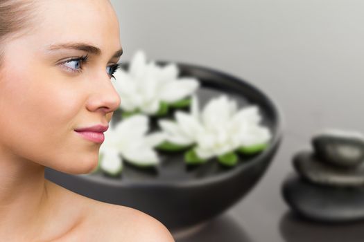 Smiling blonde natural beauty against lotus flowers floating in bowl with pebbles