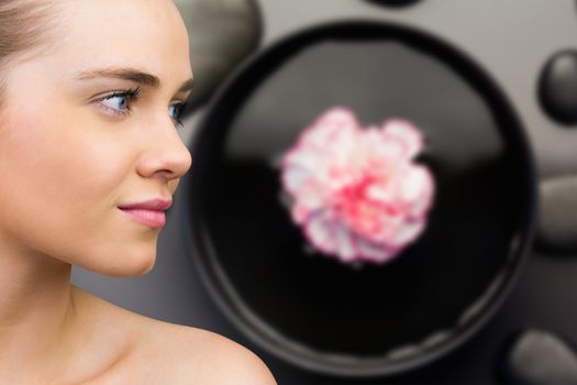 Smiling blonde natural beauty against pink flower floating in bowl with pebbles