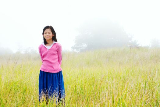 Young biracial girl quietly standing on misty foggy green field