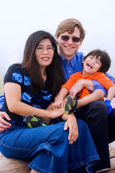 Mutiracial family sitting on beach on misty, foggy day.