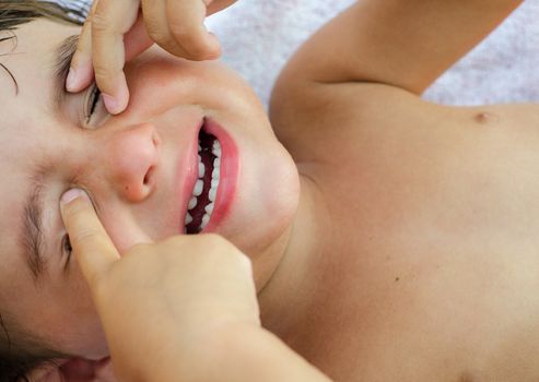 Crying baby with hands on the eyes.