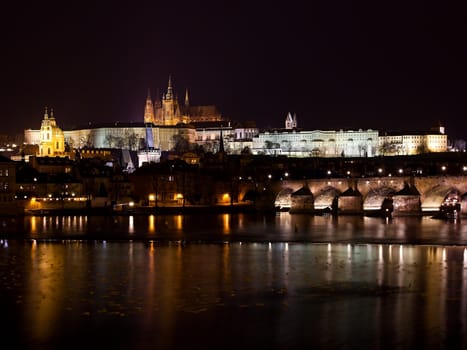 Photo shows night view of Prague Castle and bridge.
