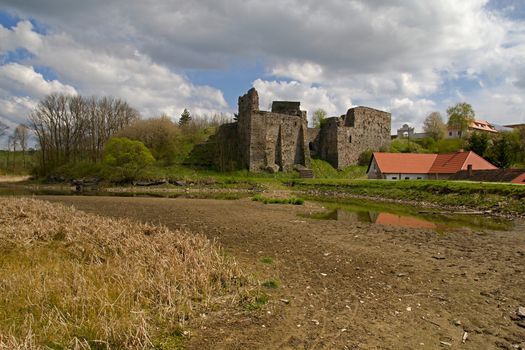 Photo shows main view of an old castle with red roof houses around.