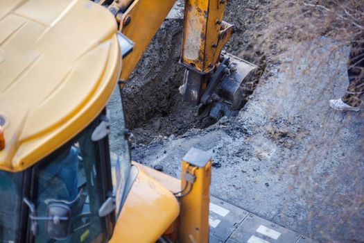Excavator digging a hole, breaking street asphalt, repairing damaged water supply pipe