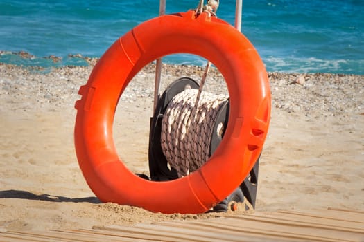 Bright an orange lifebuoy with the cable attached to it. Is at water on the bank of a sea beach.
