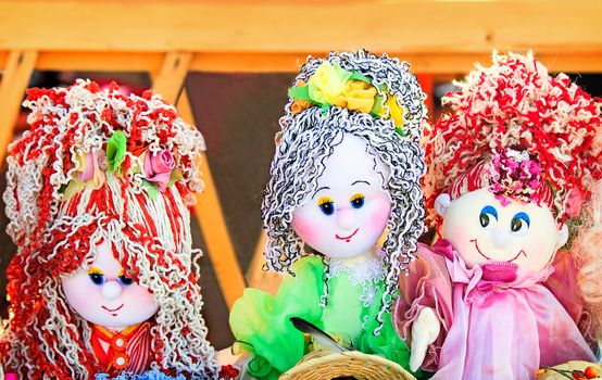 The souvenirs in the form of amusing dolls sewed from rags of fabric and laces. Are presented on a beautiful background with an embroidery.