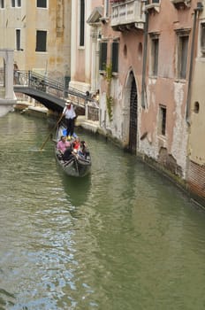 Gondola with tourists crossing a small canal in Venice, Italy