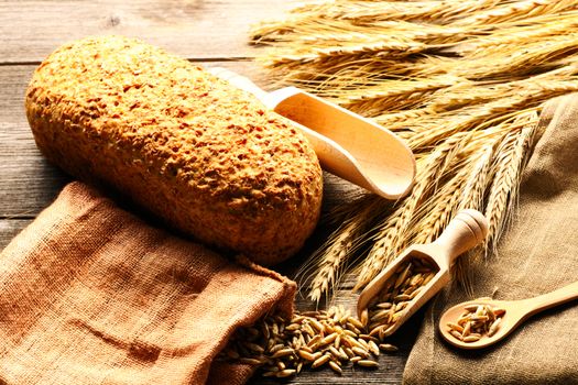 Rye spikelets and bread on wooden background