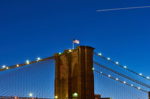 Close up of a pillar of the Brooklyn bridge with flag at night, New York City, USA