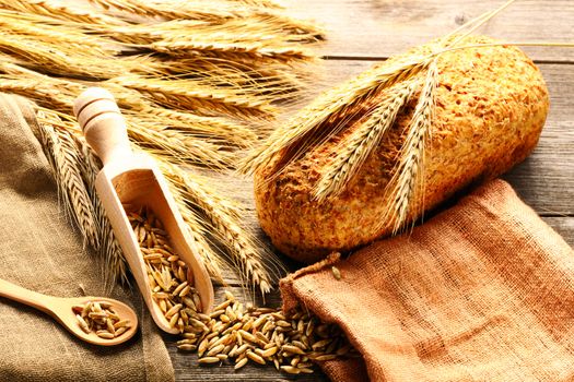 Rye spikelets and bread on wooden background