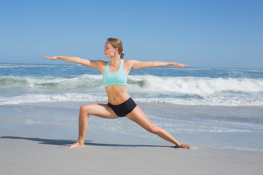 Fit woman standing on the beach in warrior pose on a sunny day