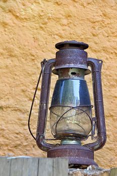 Photo shows rural lantern in front of a yellow wall.