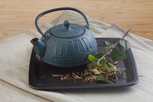 Blue iron teapot with fresh green tea branch and dried tea leaves on the black plate