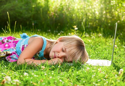 Little girl tired to use laptop and fell asleep in a summer garden