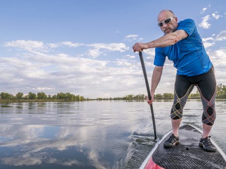 senior male paddler enjoying workout on stand up paddleboard (SUP), calm lake in Colorado, late summer
